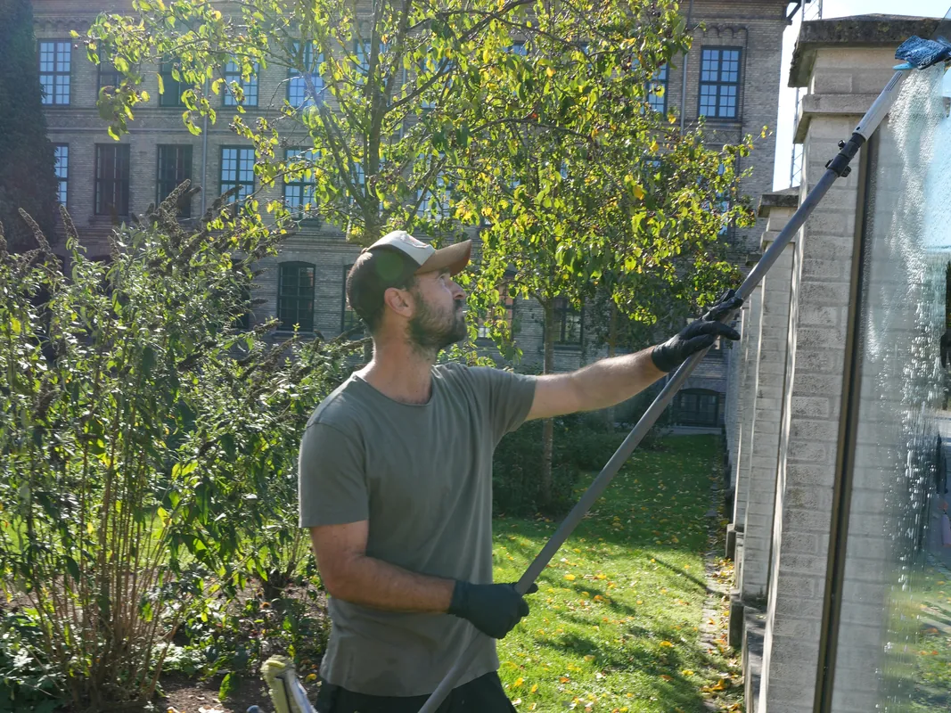 Ulrich pudser vinduer med rent vand og lang stang fra haven